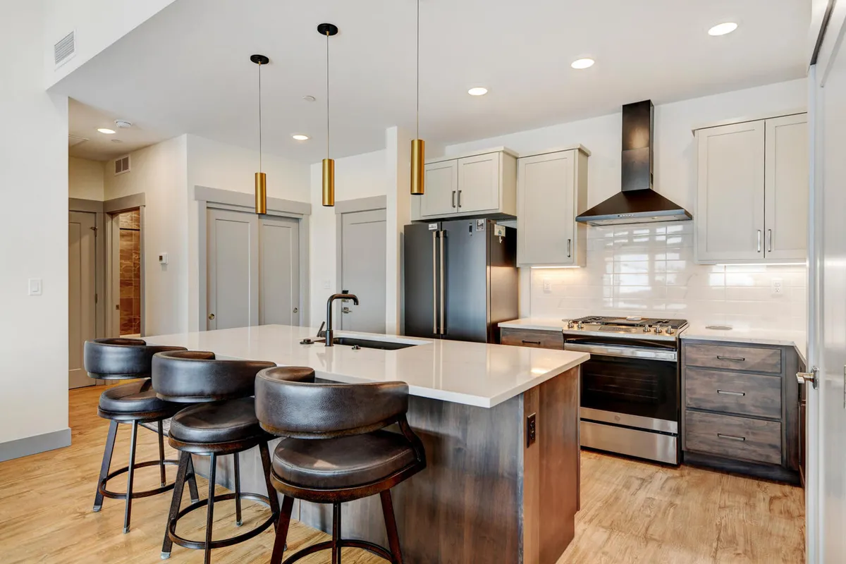 A sophisticated interior shot of a kitchen featuring a large island with bar stools, modern cabinetry, and gleaming stainless steel appliances. The space is both stylish and comfortable, inviting people to gather, cook, and dine together.