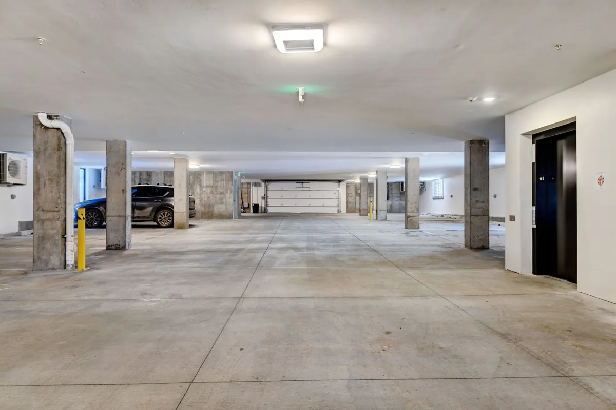 A clean, well-lit garage with concrete pillars, an elevator, and a parked car. The space feels secure and accessible, emphasizing the practical convenience of heated, secure parking for guests who bring skis, bikes, or vehicles.