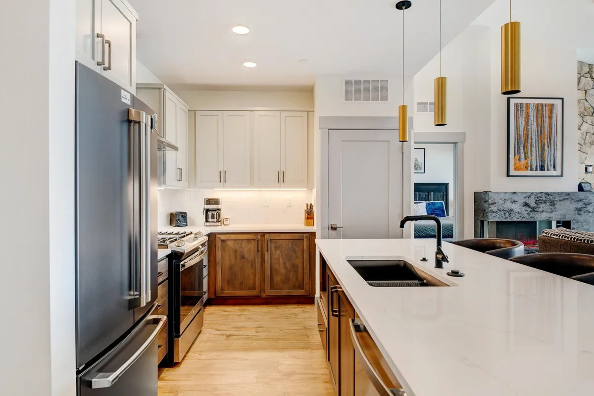 This image features a modern, inviting kitchen with stainless steel appliances, a spacious kitchen island, and striking gold pendant lights. The scene is bustling with activity, suggesting a space designed for cooking, entertaining, and social gatherings.