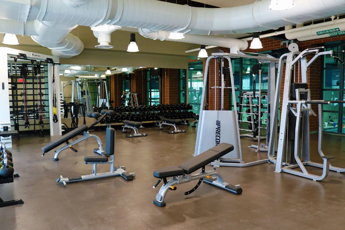 A spacious, modern gym equipped with weightlifting benches, dumbbell racks, and mirrored walls, inviting guests to pursue their fitness goals. The vibrant, motivational setting suggests active recreation just steps from the condo.