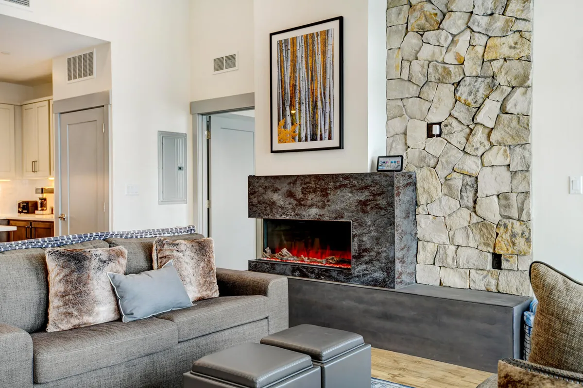 A cozy and modern living space showcases a modern fireplace as the centerpiece, complemented by a comfortable sofa and stylish artwork. The scene suggests warm, inviting evenings, perfect for après-adventure conversations or relaxing with family. The ambiance is enhanced by contemporary finishes, echoing the luxury and comfort described in the section.
