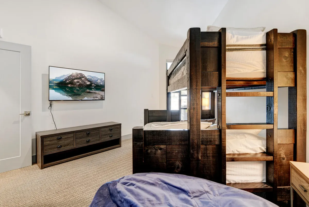 A playful yet stylish bedroom with a twin-over-queen bunk bed, a sleek dresser, and a wall-mounted TV. The setting is inviting for families or groups, offering a cozy space for kids or extra guests to unwind and enjoy movie nights together.