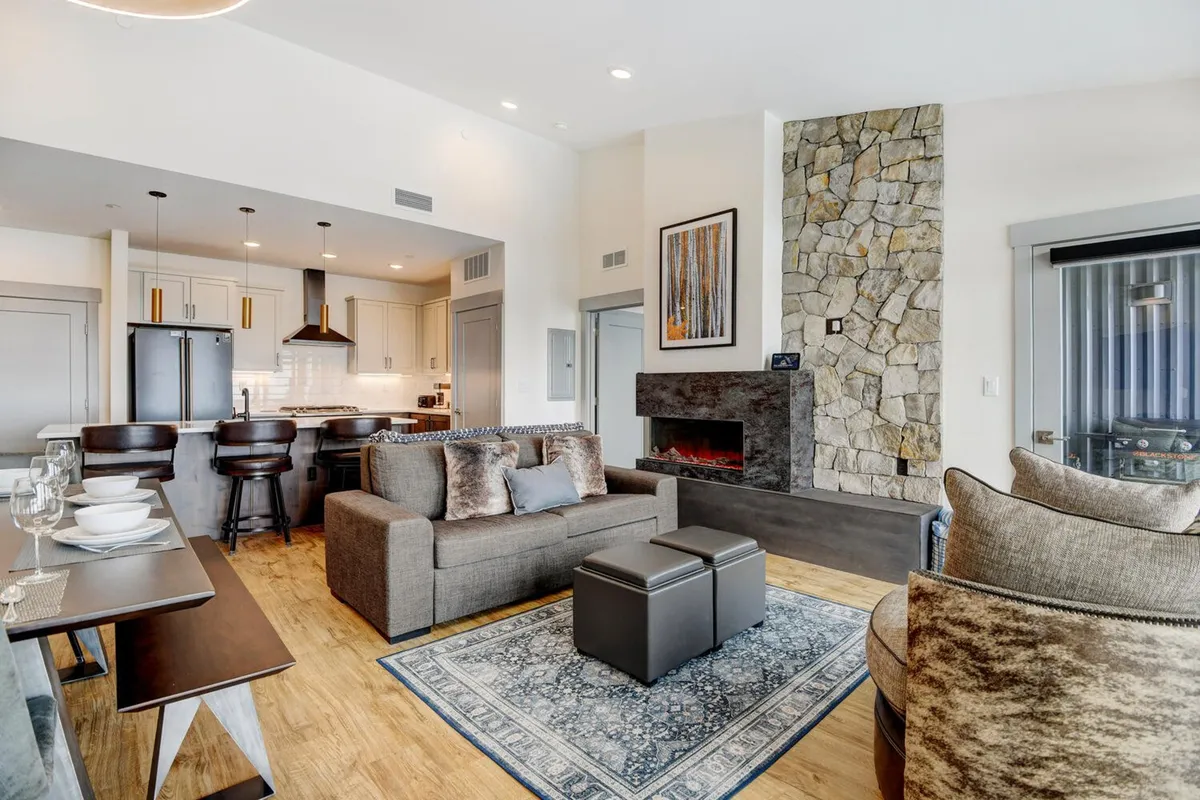 A cozy living room with a stone fireplace, plush sofa, and inviting dining table, designed for relaxation and intimate gatherings. The space exudes warmth and privacy, suggesting a perfect retreat after a day of adventure.