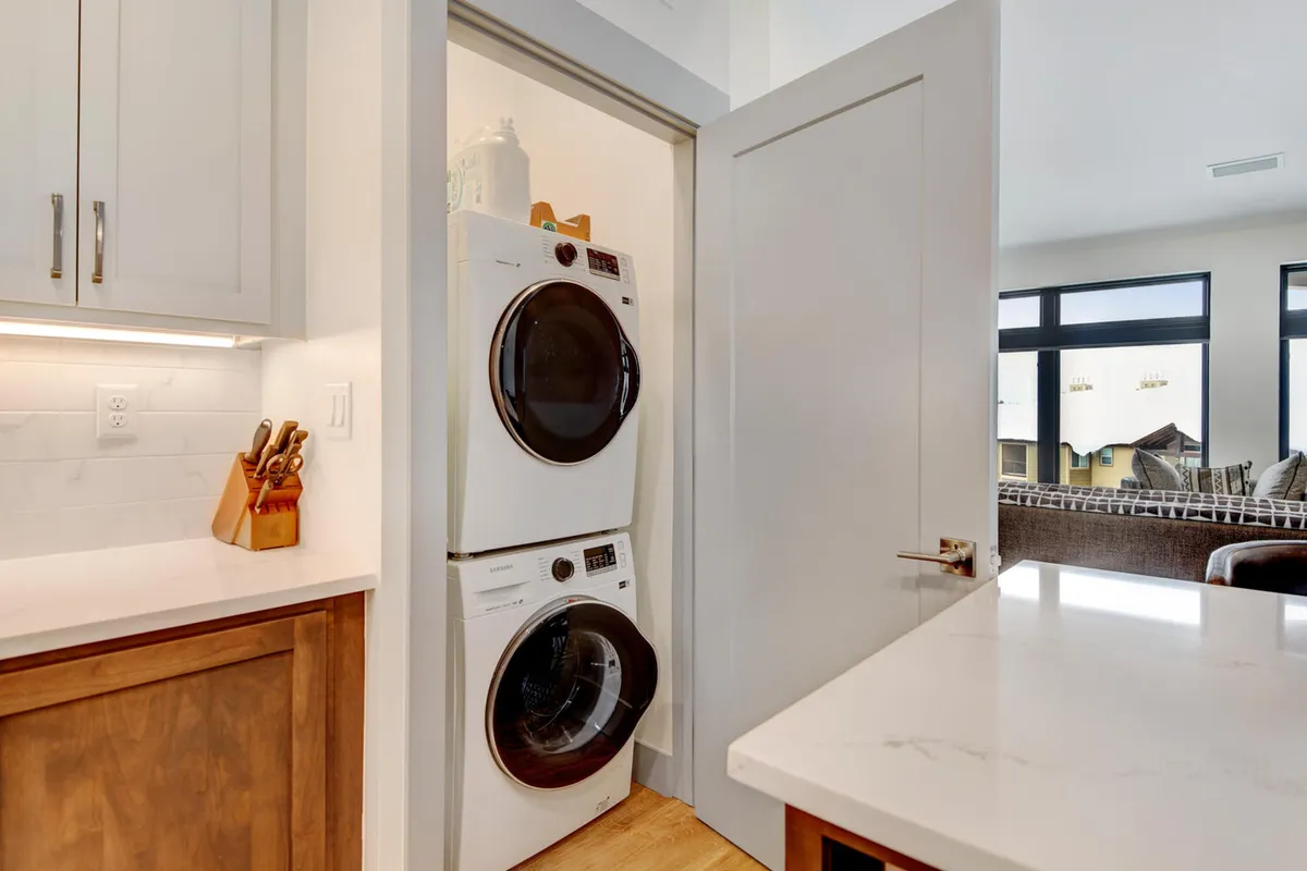 A compact, efficient laundry area with a stacked washer and dryer unit and a tidy countertop space, situated near kitchen utensils. The area is well-lit and organized, showcasing the practical conveniences available in the unit.