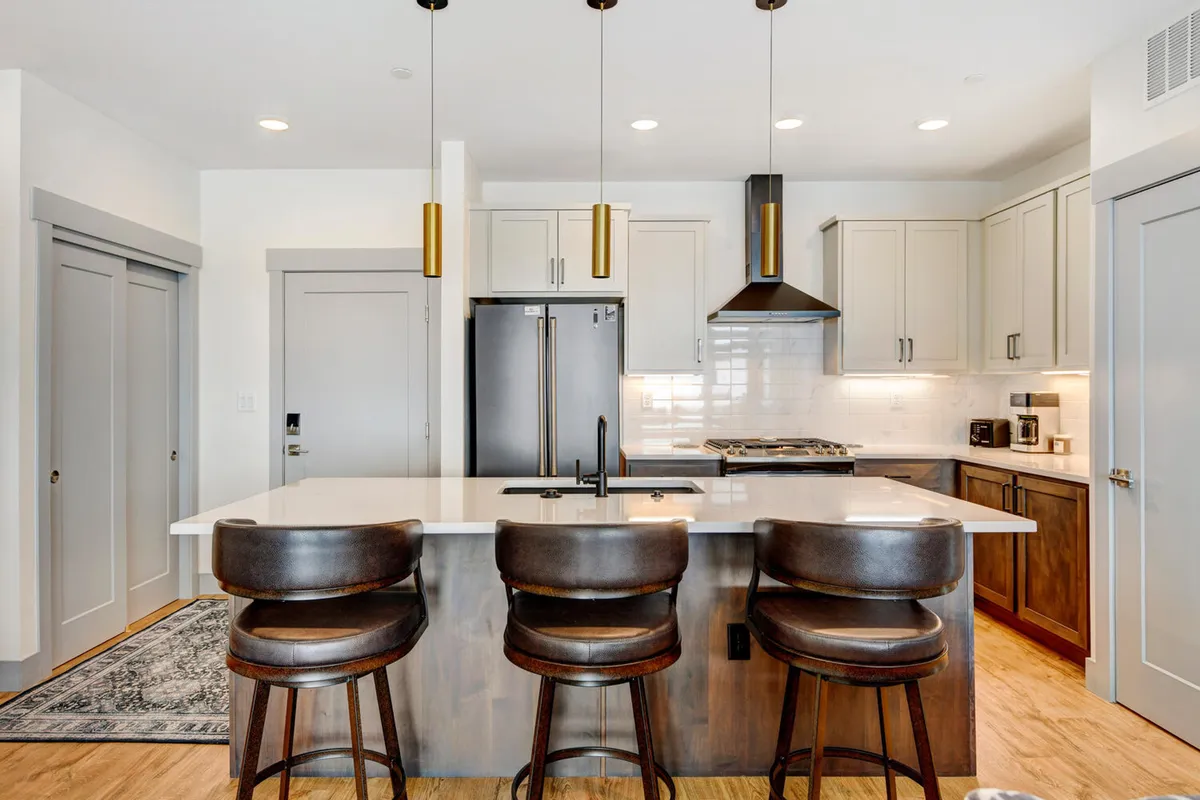 A modern, stylish kitchen highlighted by a large island with bar stools, pendant lighting, and high-end appliances. The setting feels both chic and welcoming, ideal for preparing family meals or entertaining guests.