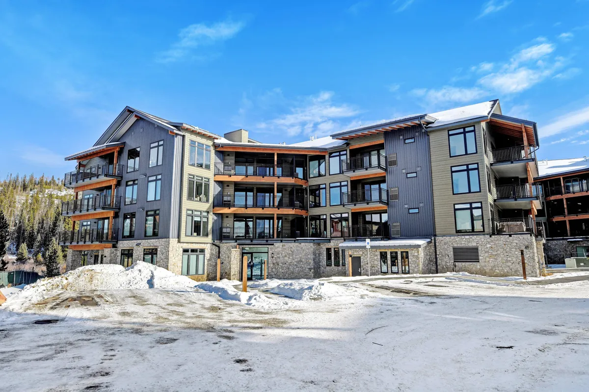The condo’s exterior with modern architecture, snow-covered ground, and large windows. Balconies offer spots for evening gatherings, and the winter environment ties into skiing and local nightlife. The scene is inviting, with hints of warmth inside the condos and the excitement of the mountain adventure outside.